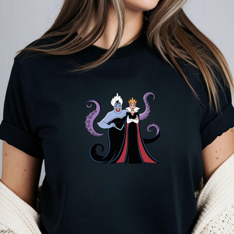 May include: Black t-shirt featuring a graphic of two cartoon villains, one with purple skin and tentacles, the other with a crown and red cape. The design is centered on the shirt, showcasing a bold and colorful illustration.