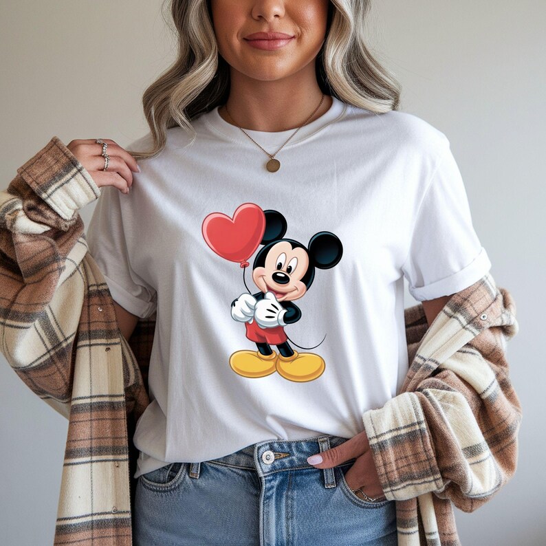 May include: White t-shirt featuring a cartoon Mickey Mouse holding a red heart-shaped balloon. Mickey is wearing red shorts, white gloves, and yellow shoes. The shirt is a classic crew neck style.