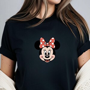 May include: Black t-shirt featuring a cartoon image of Minnie Mouse. The graphic shows Minnie's face with her signature red and white polka dot bow. The shirt is a classic crew neck style.