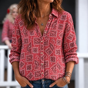 May include: A long-sleeved button-down shirt in a vibrant red hue, featuring a repeating pattern of dark paisley motifs and geometric squares. The shirt has a classic collar, a front button placket, and is paired with blue denim jeans.