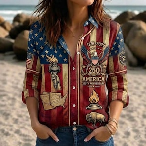 May include: A long-sleeved button-down shirt featuring a patriotic American flag print. The design includes a graphic of the Statue of Liberty torch, a map, a bald eagle with the text 1776-2026 250 AMERICA 250TH ANNIVERSARY, a flame, and a bison.