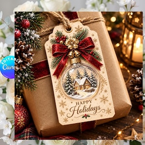 Könnte beinhalten: Ein rechteckiges beiges Geschenkanhänger-Schild mit einer Grafik einer Glaskugel, die eine verschneite Hütte und Tannenbäume zeigt. Der Anhänger ist mit einer roten Glitzerschleife, goldenen Glocken und einer goldenen Blume verziert, mit braunem Text Happy Holidays.