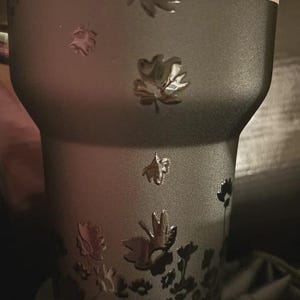 Puede incluir: Un vaso negro con un dise&ntilde;o floral en relieve. Las flores est&aacute;n en relieve sobre la superficie. El vaso tiene una etiqueta de garant&iacute;a de por vida.