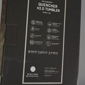 Puede incluir: Caja negra con el texto "QUENCHER H2.0 TUMBLER" e informaci&oacute;n del producto. La caja indica que el vaso contiene 1,18L y mantiene las bebidas fr&iacute;as durante 11 horas, heladas durante 2 d&iacute;as y calientes durante 7 horas.