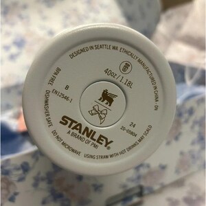 K&ouml;nnte beinhalten: Nahaufnahme des Bodens eines wei&szlig;en Stanley-Bechers. Der Boden enth&auml;lt den Text "Designed in Seattle WA", "40oz/1.18L" und "BPA Free". Das Stanley-Logo befindet sich in der Mitte.