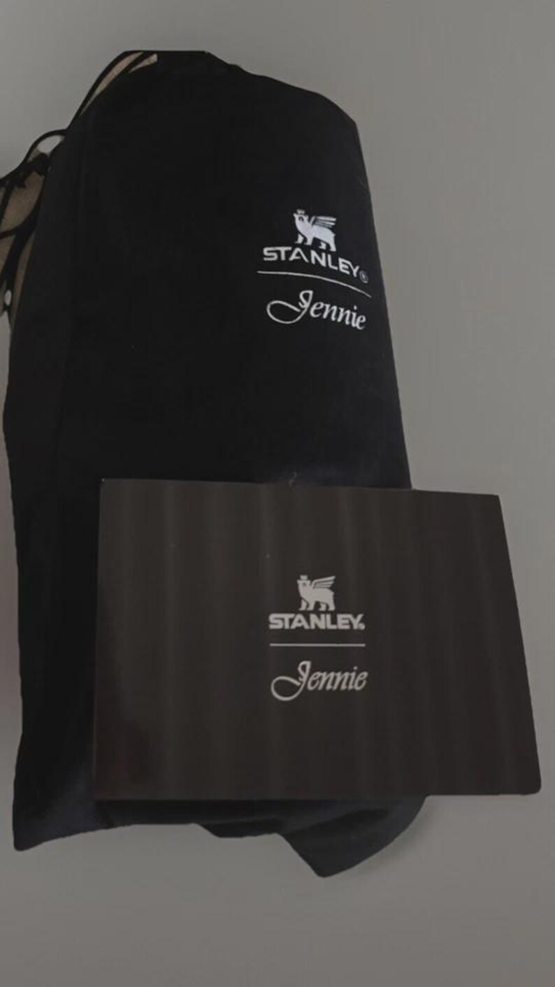 Puede incluir: Juego de bolsa y caja negros de la marca Stanley. La bolsa y la caja presentan el logotipo de Stanley y el nombre "Jennie" en escritura blanca. La caja es rectangular y parece ser de cart&oacute;n.