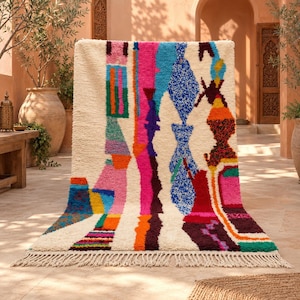 May include: A rectangular area rug with a cream-colored base featuring a vibrant, multi-colored abstract pattern of vertical stripes, geometric shapes, and textured blocks in pink, blue, orange, green, red, and purple, finished with fringe.