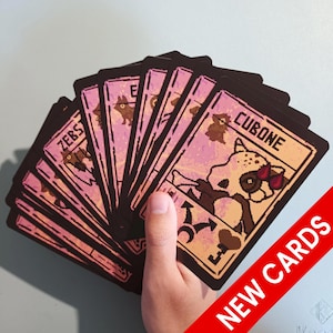 May include: A fan of rectangular trading cards with a pixelated art style, featuring a light pink background and dark borders. The top card displays the text CUBONE above a character illustration, with a heart and key icon at the bottom corner.