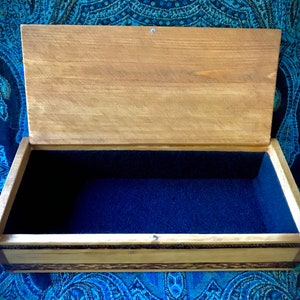 May include: A wooden box with a hinged lid and a blue velvet interior. The box has a natural wood finish and a decorative inlay around the edges.