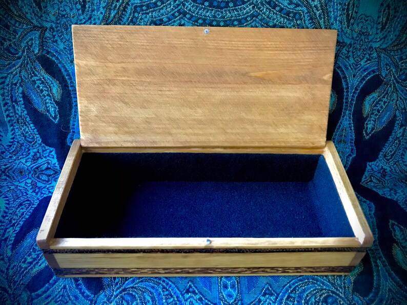 May include: A wooden box with a hinged lid and a blue velvet interior. The box has a natural wood finish and a decorative inlay around the edges.
