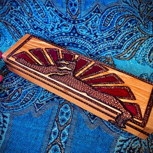May include: A wooden box with a red and copper inlay design of a stylized sunburst. The box is made of light wood and has a natural finish.