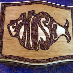 May include: A wooden box with a decorative, burnt-in design of a fish with the word "WISH" inside. The box has a dark brown border.