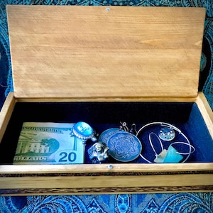 May include: A wooden box with a blue velvet interior. The box contains a &pound;20 note, a blue and silver ring, a silver bracelet, a silver necklace with a blue pendant, a blue and silver pendant, and a green stone.