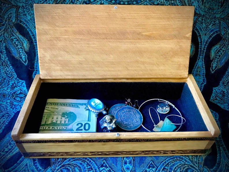 May include: A wooden box with a blue velvet interior. The box contains a &pound;20 note, a blue and silver ring, a silver bracelet, a silver necklace with a blue pendant, a blue and silver pendant, and a green stone.