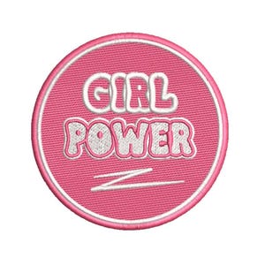 Könnte beinhalten: Ein runder, pinkfarbener, gestickter Aufnäher mit den Worten "GIRL POWER" in weißen Buchstaben im Blasenstil. Der Aufnäher hat einen weißen Rand und eine weiße Zickzacklinie. Auf weißem Hintergrund.