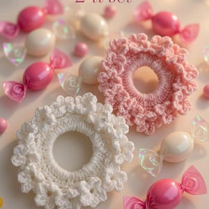 May include: Two crochet scrunchies, one white and one pink, with a ruffled edge, are displayed with candy-shaped decorations. The text "2'li set" is visible. The candy is pink and white with clear cellophane wrappers.