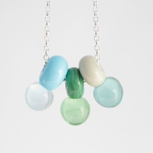 Puede incluir: Un collar de cadena de plata con un grupo de cuentas de vidrio azul pastel, verde y blanco.