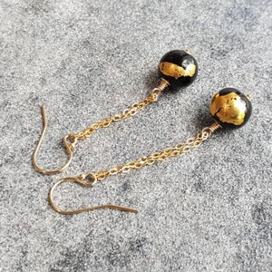 May include: A pair of gold chain earrings with black and gold round beads. The beads have a textured surface and gold flecks.