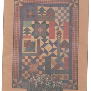 May include: A patchwork quilt with a variety of geometric shapes and patterns in shades of blue, red, green, and tan. The quilt features stars, trees, and floral motifs, framed by a plaid border. The quilt is displayed with a floral arrangement.