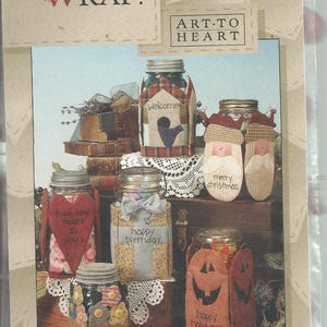 May include: A craft pattern booklet titled IT'S A WRAP! ART TO HEART Pattern #1 featuring six glass jars decorated with fabric covers. Designs include a birdhouse, Santa Claus, a red heart, a gift box, flowers, and a jack-o'-lantern with text.