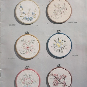 May include: A page from "J.D.R. Brazilian Embroidery Book I" featuring six embroidered floral designs in round hoops. The designs include Cross-Needle Hydrangeas, Creeping Flower, Gerone Daisy, Lazy Daisy, Rolled Rose, and Peach Blossom.