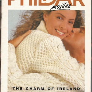 May include: Magazine cover featuring a woman wearing a cream-colored, textured sweater with a turtleneck. The text "PHILDAR mailles" is at the top, with "THE CHARM OF IRELAND IN EVERY SWEATER" below. A person is kissing the woman on the cheek.