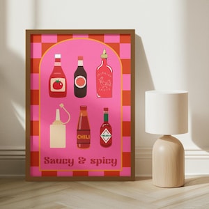 Puede incluir: Un estampado enmarcado con un fondo rosa y el texto "Saucy & Spicy". El estampado presenta ilustraciones de seis botellas de salsa, incluyendo ketchup, salsa de soja y Tabasco. El fondo tiene un patrón de cuadros rojos y rosas. El marco es marrón.