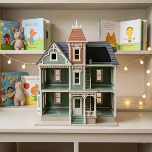 Puede incluir: Una casa de mu&ntilde;ecas de varios pisos con revestimiento verde salvia, techo de tejas gris oscuro y una torre central con techo color terracota. La estructura incluye marcos de ventanas blancos, un porche delantero con escaleras.