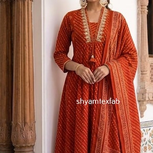 Puede incluir: Un conjunto de kurta de manga larga color naranja óxido con un patrón de puntos diagonales blancos, escote en V con bordado dorado y un dupatta a juego con borde geométrico. El texto shyamtexfab es visible en la prenda.