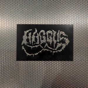 May include: A black rectangular sticker with the word "EGOISTS" in a silver, dripping font. The sticker is set against a textured, silver background.