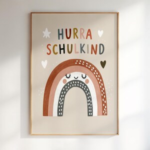 Könnte beinhalten: Ein rechteckiger Wanddruck auf beigem Hintergrund mit dem Text HURRA SCHULKIND in bunten Buchstaben. Unter dem Text befindet sich eine stilisierte Regenbogenillustration mit einem lächelnden Gesicht, geschlossenen Augen und braunen Punkten.