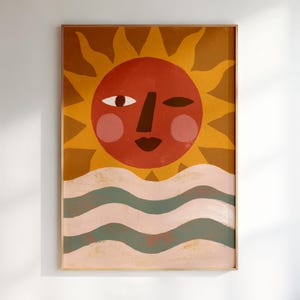 May include: A rectangular wall art print featuring a stylized sun with a terracotta face, pink cheeks, and a dark brown nose and lips. The sun is set against a mustard yellow background with rays, positioned above wavy horizontal stripes of sage green and cream.