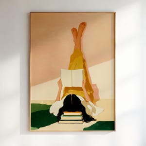 May include: A framed art print depicts a person lying down, reading a book with their legs raised. The person is wearing yellow pants and a white top. A stack of books is at the bottom. The background is a mix of peach, white, and green.