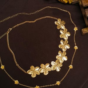 May include: A gold-toned metal waist chain featuring a cluster of six textured floral charms on one side and smaller individual flower accents spaced along the delicate link chain, which includes an adjustable clasp closure for a custom fit.