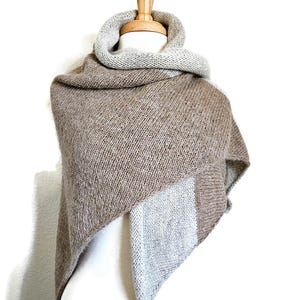 May include: A triangular knitted shawl in brown and light grey with a textured knit pattern. The shawl is draped over a mannequin.