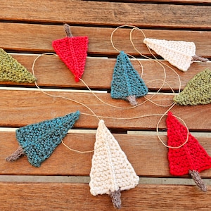 May include: A garland of knitted Christmas trees in red, green, white, and blue. The trees are strung together with twine and are hanging on a wooden surface.