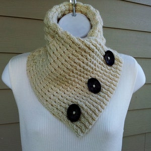 May include: A cream-colored knitted cowl neck scarf with three black buttons.