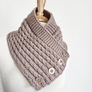 May include: A brown knitted cowl neck scarf with a button closure. The scarf is folded over and has a textured knit pattern.