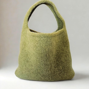 Könnte beinhalten: Eine grüne, strukturierte Tragetasche mit einem einzigen Griff. Die Tasche hat eine einfarbige olivgrüne Farbe und einen abgerundeten Boden. Der Griff ist gewölbt und oben an der Tasche befestigt.