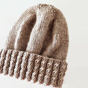May include: A brown knitted beanie with a ribbed brim. The beanie is made of a soft, warm yarn.