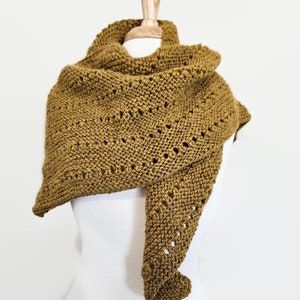 以下が含まれることがあります： マスタードイエローのクロシェ編みショールで、繊細な透かし模様が施されています。ショールは白いマネキンにかけられています。