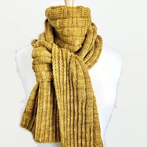 May include: A mustard yellow knitted scarf with a cable knit pattern. The scarf is folded and draped over a white mannequin.