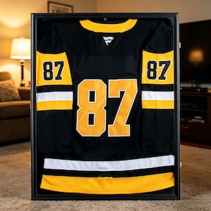 May include: Framed black hockey jersey with yellow and white accents. The jersey features the number 87 in large yellow numerals on the front, sleeves, and back. The jersey is displayed in a black frame.