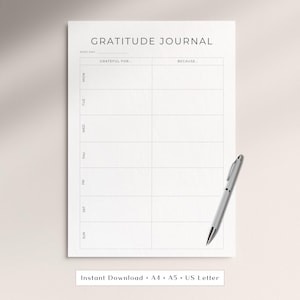 May include: A white gratitude journal page with black text and lines. The header reads GRATITUDE JOURNAL, followed by columns labelled GRATEFUL FOR and BECAUSE, and rows for each day of the week from MON to SUN. A silver pen rests on the paper.