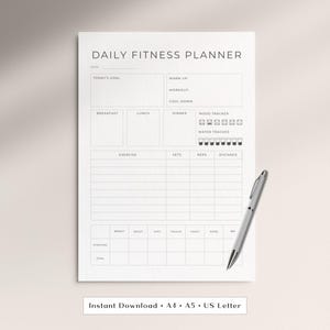 Könnte beinhalten: Ein weißer täglicher Fitnessplaner mit schwarzem Text und Linien. Er enthält Abschnitte für Ziele, Aufwärmen, Training, Cool-down, Mahlzeiten, Stimmungs- und Wassertracker, ein Übungsprotokoll und Körpermaße. Ein silberner Stift liegt auf der rechten Seite.