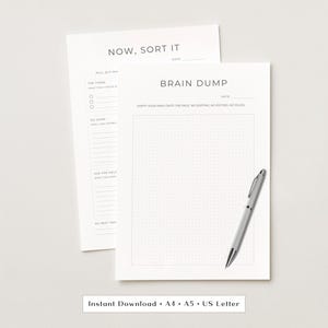 May include: Two white paper sheets with black text and a silver pen. The top sheet is titled BRAIN DUMP with a dot grid section and the text EMPTY YOUR MIND ONTO THE PAGE. NO SORTING, NO EDITING, NO RULES. The sheet behind is titled NOW, SORT IT.
