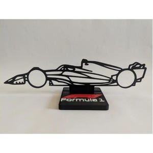 Peut inclure: Une silhouette noire, plate et filaire d'une voiture de course de Formule 1 montée sur une base rectangulaire noire. La base présente le logo rouge et blanc de la Formule 1 imprimé sur sa face avant. L'objet est fait d'un matériau rigide et fin.