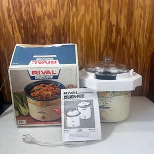 May include: A vintage Rival Crock-Pot slow cooker with its original box and manual. The box features an image of cooked food. The slow cooker is cream-colored with floral accents and a clear lid. The power cord is visible.
