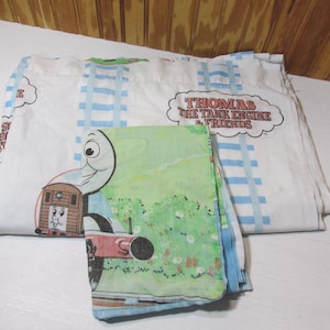 May include: A white twin-sized bed sheet with a blue and white striped border. The sheet features a cartoon image of Thomas the Tank Engine and his friends. The sheet also includes a smaller pillowcase with a green and blue design featuring Thomas the Tank Engine.
