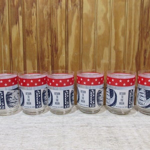 May include: Set of six clear glass tumblers with a red and white band of stars and a blue and white image of the Apollo 12 mission. The image says "Return to the Moon, November 19, 1969".